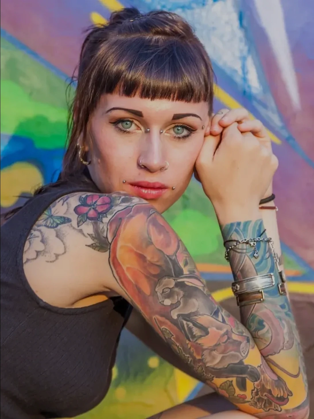 Tattooed woman posing against colorful graffiti.