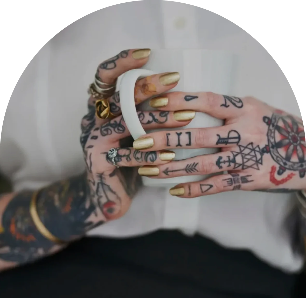 Tattooed hands holding a white coffee mug.